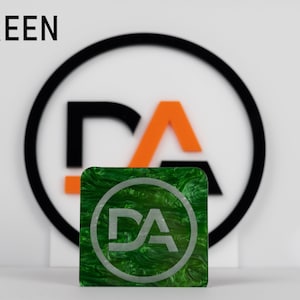 May include: Green square with a swirling pattern and a white circle with the letters "DA" in the center. The square is in front of a black circle with a white "DA" logo inside.