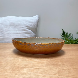 May include: A large, brown ceramic bowl with a textured, speckled glaze. The bowl has a slightly wavy rim and is sitting on a wooden surface.