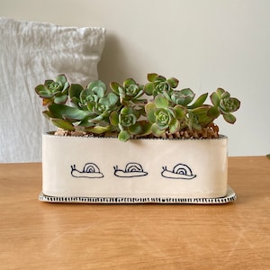Peut inclure: Ensemble de trois tasses en céramique avec une finition mate et mouchetée. Les tasses sont de couleur crème, gris clair et gris foncé. Chaque tasse a un design simple et minimaliste et une anse arrondie.