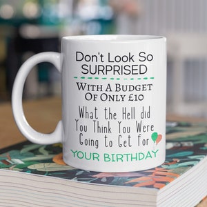 May include: White ceramic mug with a funny birthday message that reads "Don't Look So Surprised With A Budget Of Only £10 What the Hell did You Think You Were Going to Get for YOUR BIRTHDAY".