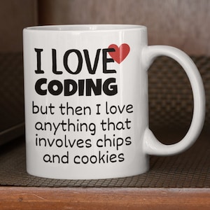 May include: White ceramic coffee mug with black text that reads "I love coding but then I love anything that involves chips and cookies". A red heart is next to the word "love".