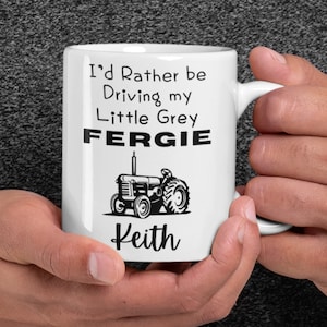 Può includere: Una tazza in ceramica bianca con un design nero che dice "I'd Rather be Driving my Little Grey FERGIE" con un'illustrazione in bianco e nero di un trattore. Il nome "Keith" è stampato sotto il trattore.
