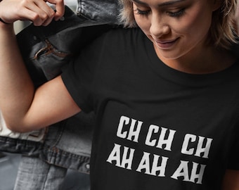 May include: A black t-shirt with white text that reads "CH CH CH AH AH AH". The person wearing the shirt is standing in a city setting.