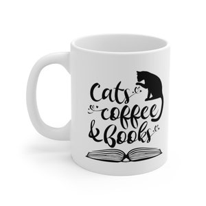 May include: White ceramic coffee mug with a black silhouette of a cat, an open book, and the text "Cats, coffee & books".
