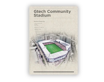 May include: An artistic print of the Gtech Community Stadium, home of Brentford Football Club, with the stadium's name at the top. The stadium is depicted with a green pitch and white roof, surrounded by buildings. The print has a textured, off-white background.