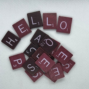May include: A collection of brown and purple letter tiles spelling out the word "HELLO" in a white background. The tiles are from a Scrabble game.