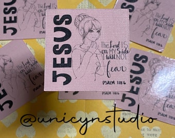May include: Pink square stickers with the word "JESUS" in large black letters. Each sticker features a sketch of a girl and the text "The Lord is on my side, I will not fear" with a Bible verse reference.