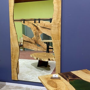 May include: A large, rectangular mirror with a natural wood frame. The frame has a unique, organic shape with a live edge. The mirror is reflecting a room with a wooden table and a rug.