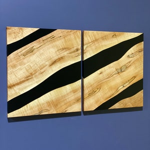 May include: Two wooden wall art panels with black resin flowing through the wood grain. The panels are rectangular and have a natural wood finish.
