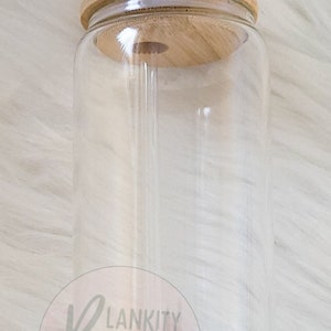 May include: A clear glass tumbler with a bamboo lid and a clear straw. The tumbler has a cylindrical shape and is designed for cold drinks. The lid has a hole for the straw. The logo "BLANKITY BLANKS" is visible on the bottom.