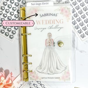 May include: A wedding savings challenge binder with gold-coloured hardware. The cover displays the text "SABRINAS' WEDDING Savings Challenge" and a bride illustration. The image also includes stickers and the text "MATTE VELLUM COVER 4 COVER VARIATION!"