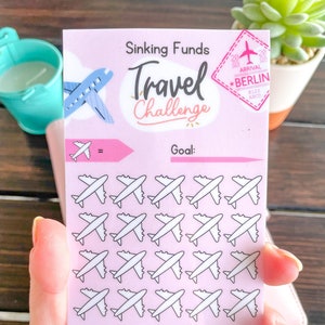 Può includere: Tracker di viaggio stampabile rosa con un'icona di aereo e il testo "Sinking Funds Travel Challenge". Il tracker ha una sezione di obiettivi con 30 icone di aereo da colorare mentre risparmi per il tuo viaggio. Il tracker ha anche un adesivo con il testo "Arrival Berlin" e un altro adesivo con il testo "Arrival Tokyo".