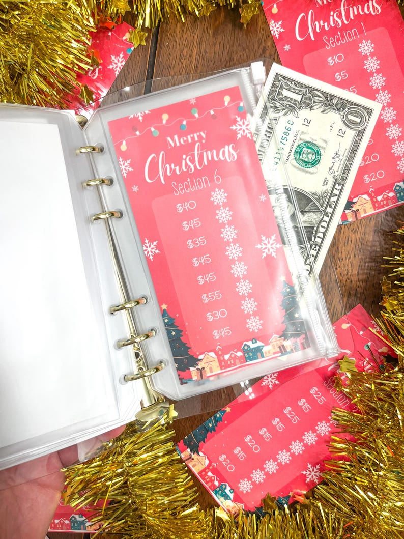 Pode incluir: Um fich&aacute;rio de pl&aacute;stico transparente com um inserto de tema natalino vermelho e branco. O inserto tem um t&iacute;tulo que diz "Feliz Natal Se&ccedil;&atilde;o 6" e lista v&aacute;rios valores em euros. Uma nota de um euro &eacute; vis&iacute;vel no fich&aacute;rio.