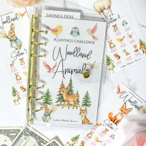 Peut inclure: Un classeur en plastique transparent avec des anneaux dorés et une fermeture à pression, présentant une couverture Woodland Animal 1K Savings Challenge. L'ensemble inclut des inserts assortis illustrés de cerfs, lapins, renards et oiseaux.