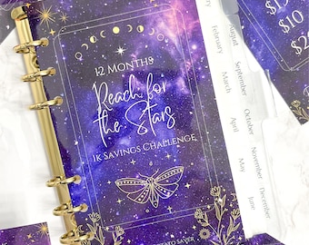 May include: A purple and gold savings challenge binder with the text "Reach for the Stars" and "1K Savings Challenge". The binder has gold rings and monthly dividers. Additional cards with savings amounts are visible.