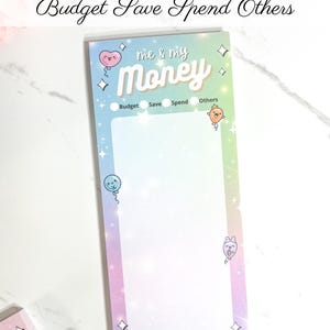 May include: A rectangular money note pad with the text "MONEY NOTE PAD" and "Budget Save Spend Others". The pad has a pastel rainbow gradient background with the words "me & my Money". It includes sections for Budget, Save, Spend, and Others.