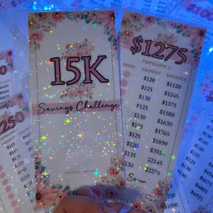 May include: A pink and white savings challenge card with a glittery background and stars. The card has the text "15K Savings Challenge" and a chart with amounts and balances for a savings goal of £1275.