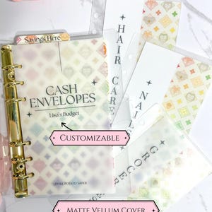 May include: A gold binder with matte vellum covers and customizable cash envelopes. The envelopes are decorated with a geometric pattern and labeled for categories like "Hair Care" and "Groceries".