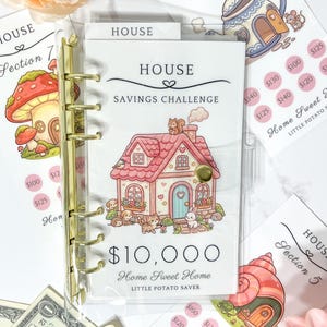 May include: A clear plastic binder with gold rings featuring a House Savings Challenge insert. The cover displays a pink house illustration, a squirrel, a cat, and a rabbit, with the text $10,000 Home Sweet Home Little Potato Saver.