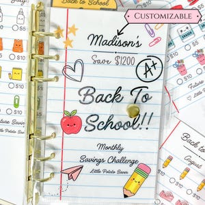Peut inclure: Un classeur A6 en plastique transparent avec des anneaux dorés présentant un motif de papier ligné. La couverture affiche le texte Madison's Save $1200 Back To School!! Monthly Savings Challenge, avec des illustrations de pomme, crayon et avion.