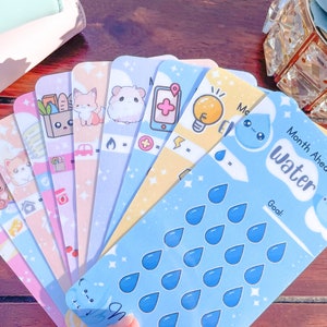 Pu&ograve; includere: Una collezione di colorate schede planner con simpatiche illustrazioni. Le schede presentano vari disegni, tra cui animali, cibo e icone. Una scheda ha il testo "Month Ahead Water" con grafiche a goccia d'acqua.