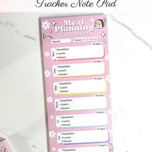 May include: A pink meal planning expense tracker notepad with the text "Meal Planning Expense Tracker Note Pad." The notepad has sections for each day of the week, with spaces for breakfast, lunch, and dinner, and a budget section.