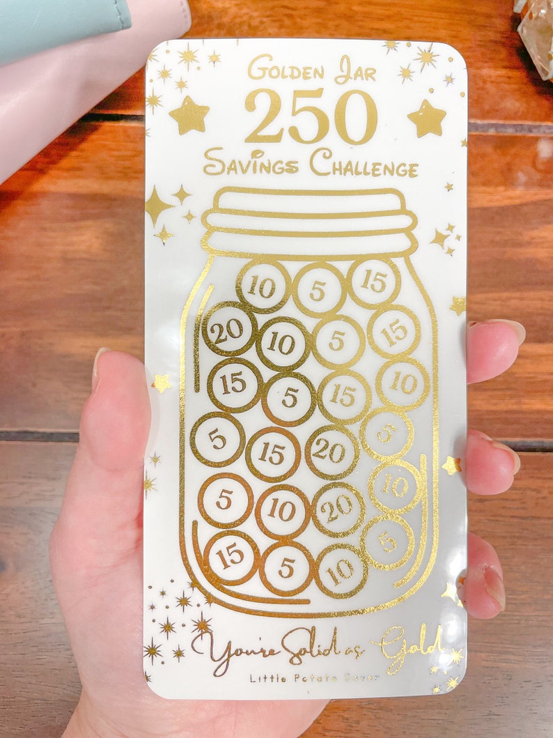 May include: A white card with gold lettering and a gold jar illustration. The card says "Golden Jar 250 Savings Challenge". The jar is filled with gold coins with numbers on them, such as 5, 10, 15, and 20. The card also says "You're Solid as Gold" and "Little Payam Studio".