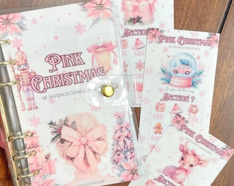May include: A clear binder with gold rings and a snap closure, featuring pink Christmas-themed inserts. The inserts include illustrations of a gift, snow globe, and a deer, with text reading "Pink Christmas" and "5K Savings Challenge."