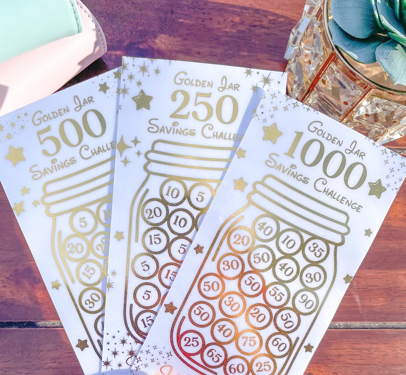 May include: Three gold foil printed cards with a savings challenge theme. Each card features a mason jar with coins inside and a gold star. The cards are labeled "Golden Jar 500 Savings Challenge", "Golden Jar 250 Savings Challenge", and "Golden Jar 1000 Savings Challenge".