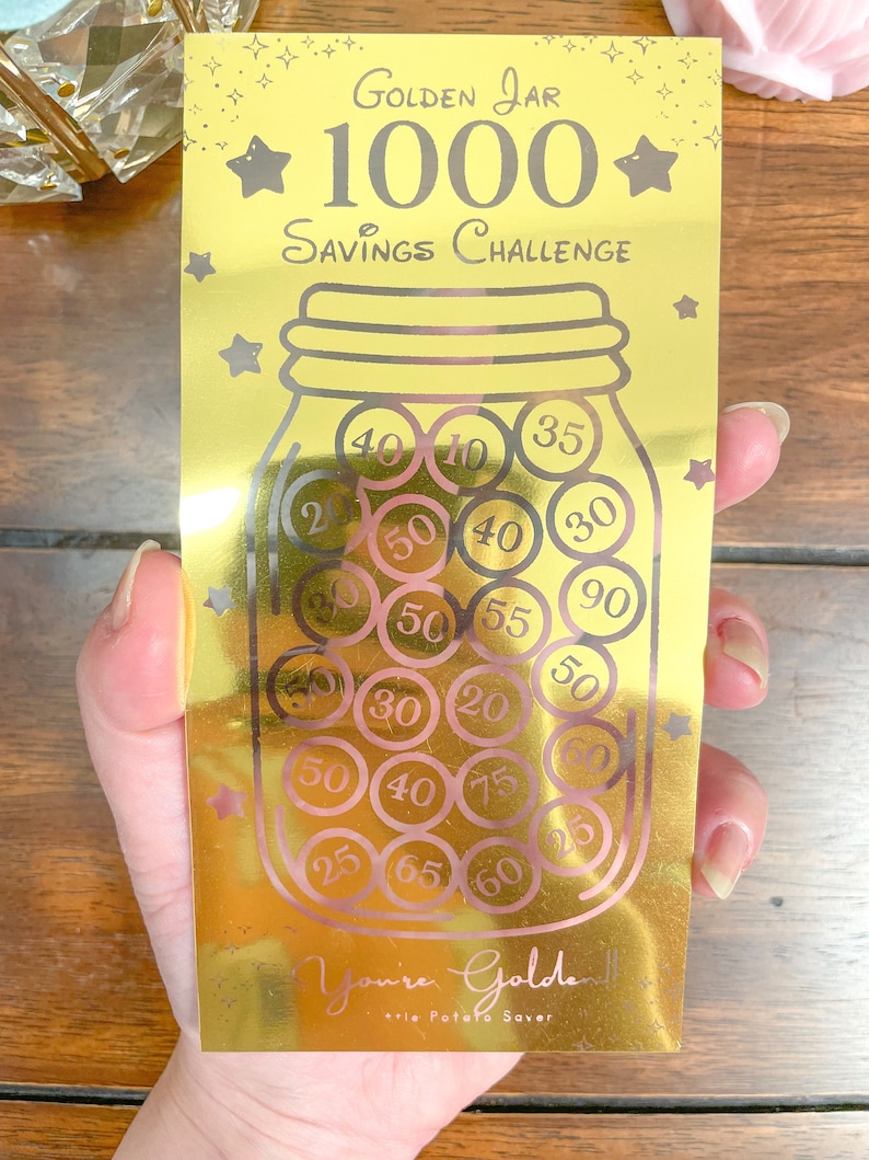 May include: Gold savings challenge jar with a gold background and a gold lid. The jar is filled with pink and black coins with numbers on them. The text on the jar reads "Golden Jar 1000 Savings Challenge".