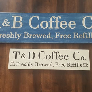 May include: Two wooden signs with the text "A&B Coffee Co. Freshly Brewed, Free Refills" and "T&D Coffee Co. Freshly Brewed, Free Refills" on them. Both signs have a coffee cup icon with steam coming from it.