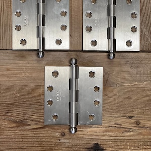 May include: Three silver ball-tipped door hinges with the text "EMTEK" and "ASSEMBLY" on each hinge.
