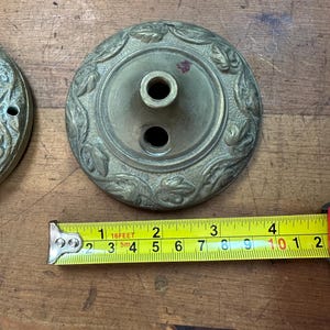 Puede incluir: Un par de medallones de techo decorativos de latón antiguo. Los medallones redondos tienen un agujero central y dos agujeros más pequeños. El borde exterior presenta un diseño detallado de hojas y vides. El diámetro es de aproximadamente 10 cm.