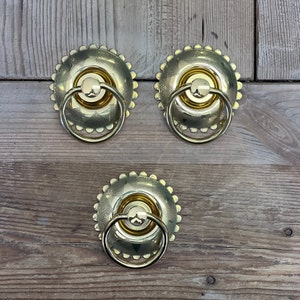 May include: Three gold-toned door knobs with a decorative, patterned design. Each knob has a ring handle.