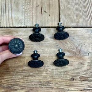 May include: Five black metal cabinet knobs with a floral design. The knobs have a silver screw in the center.