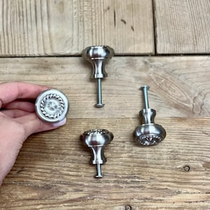 May include: Three silver cabinet knobs with a rope design around the edge. The knobs have a round base and a small stem with a screw.