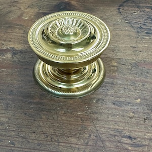 May include: A gold-toned door knob with a decorative, raised, circular design.