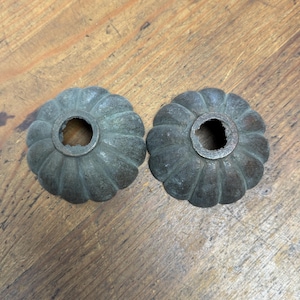 Puede incluir: Dos pomos de metal de color bronce antiguo con un diseño acanalado en forma de calabaza. Cada pomo tiene un agujero central. Los pomos se muestran sobre una superficie de madera envejecida.