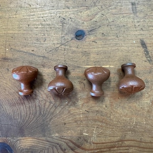 May include: Four brown cabinet knobs with a textured finish are arranged on a wooden surface. The knobs have a rounded top with a decorative pattern and a cylindrical base. The wood grain is visible in the background.