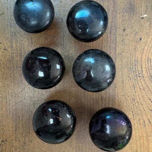 May include: Six black, spherical objects with a glossy finish are arranged on a wooden surface. The spheres reflect light, displaying hints of blue and purple. The objects appear to be decorative or functional, possibly knobs or drawer pulls.