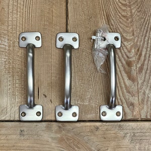 May include: Three brushed nickel cabinet pulls with a rectangular base and a curved handle. One pull includes screws in a plastic bag. The pulls are displayed on a light brown wooden surface.