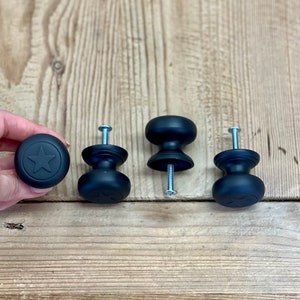 May include: Four black cabinet knobs with a star design. The knobs are made of metal and have a matte finish.