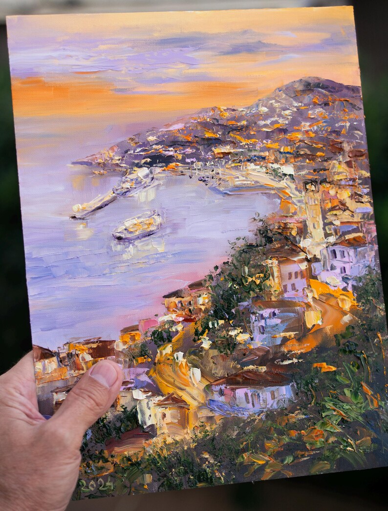 Puede incluir: Una pintura de una ciudad costera con un puerto y barcos. La ciudad est&aacute; construida en una ladera y los edificios est&aacute;n pintados en tonos de amarillo, naranja y marr&oacute;n. El cielo es de un suave p&uacute;rpura y naranja.