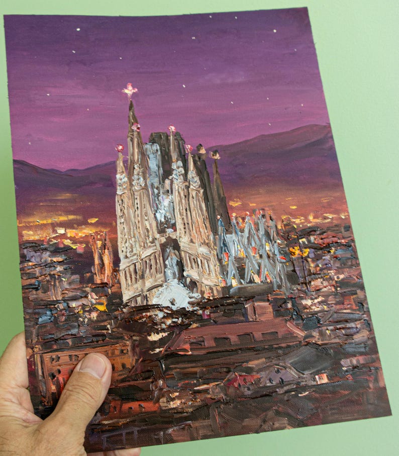 May include: An oil painting on a rectangular canvas depicting the Sagrada Familia at twilight. The scene features the cathedral's spires against a deep purple sky with stars, overlooking a city landscape rendered in dark brown, orange, and yellow.