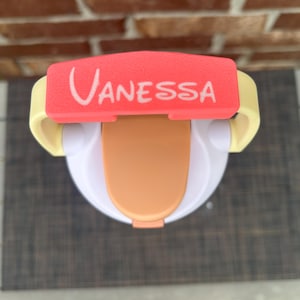 Op de afbeelding: Een witte en oranje tuitbeker met een rode deksel met de naam "Vanessa" in witte letters. De beker heeft gele handvatten en een lichtoranje tuit. Deze tuitbeker is ontworpen voor peuters en jonge kinderen.