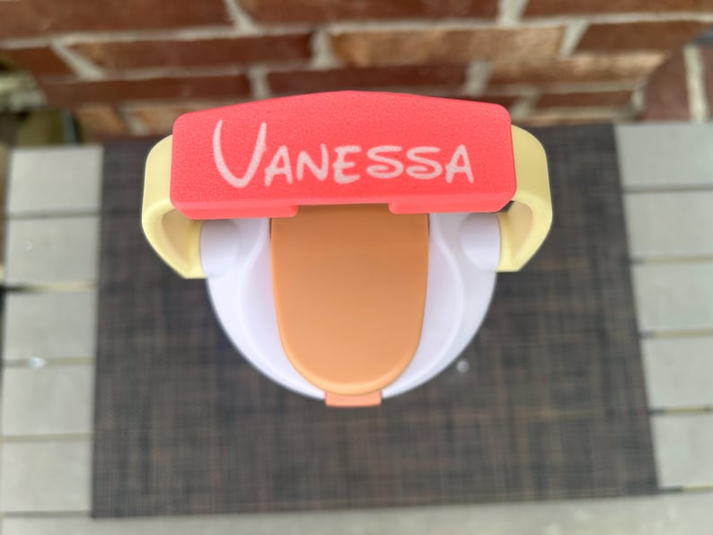 Op de afbeelding: Een witte en oranje tuitbeker met een rode deksel met de naam "Vanessa" in witte letters. De beker heeft gele handvatten en een lichtoranje tuit. Deze tuitbeker is ontworpen voor peuters en jonge kinderen.