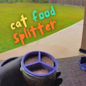 May include: A close-up of a blue and white cat food splitter with three sections. The splitter is filled with brown cat food. The text "cat food splitter" is written in colorful letters on a green grassy background.