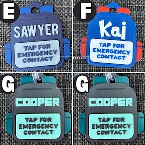 May include: A collection of backpack-shaped luggage tags in blue, red, and gray. Each tag features a name: "Sawyer", "Kai", or "Cooper", and the text "TAP FOR EMERGENCY CONTACT". The tags have a loop for attachment.