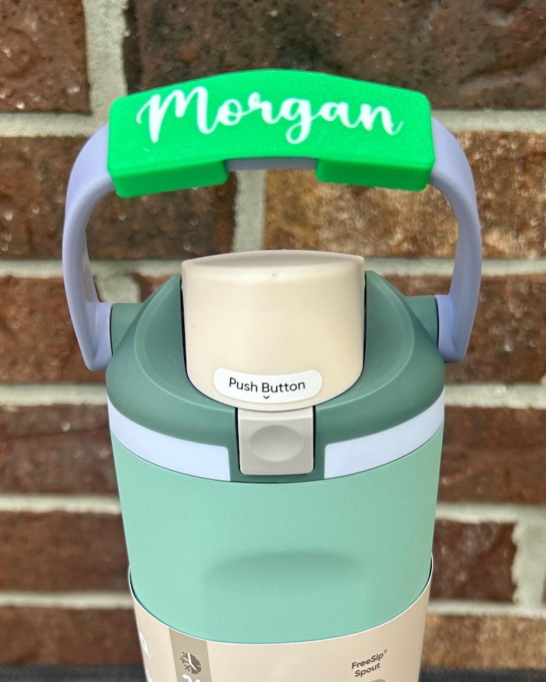 Op de afbeelding: Een turquoise en grijze waterfles met een groene handgreep met de naam "Morgan" in witte letters. De fles heeft een drukknop en een "FreeSip" tuit.