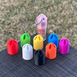 Peut inclure: Assortiment de dix bouchons de bouteille en plastique color&eacute;s avec trois trous chacun. Les bouchons sont en rouge, blanc, noir, orange, vert, bleu et rose. Une petite bouteille transparente avec un bouchon rose et un porte-cl&eacute;s argent&eacute; se trouve en arri&egrave;re-plan. La bouteille porte le texte "Real Salt".